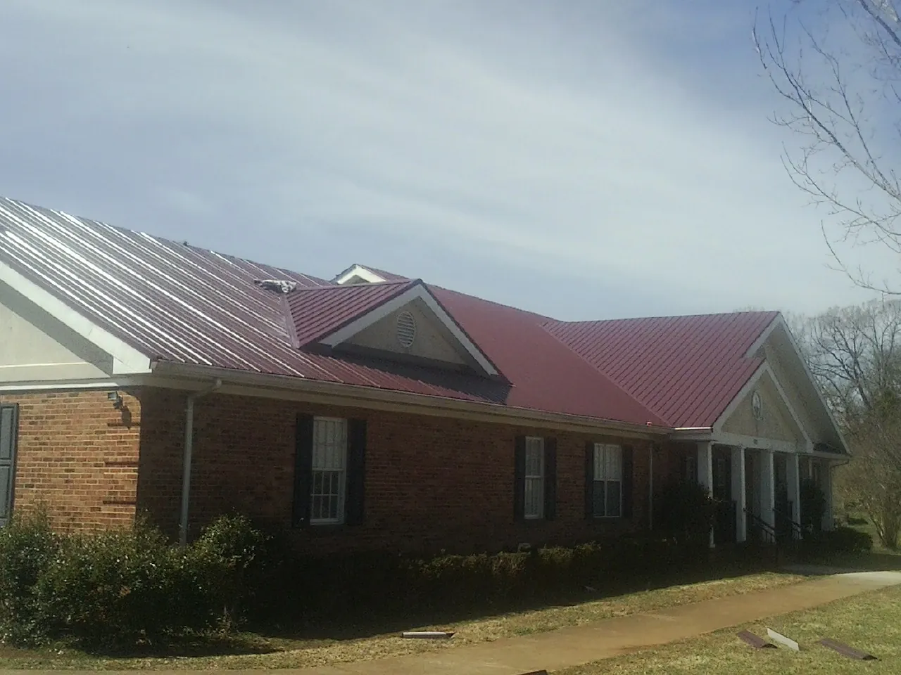 Red metal roof with gabled entries on a long brick building, from a Hail Damage Roof Repair job in Nashotah