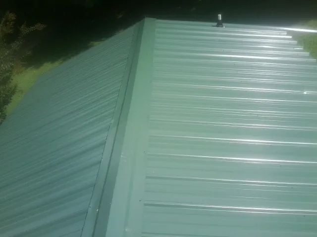 New green metal panels meeting at the ridge of a roof — Flat Roof Repair work by our crew in Nashotah