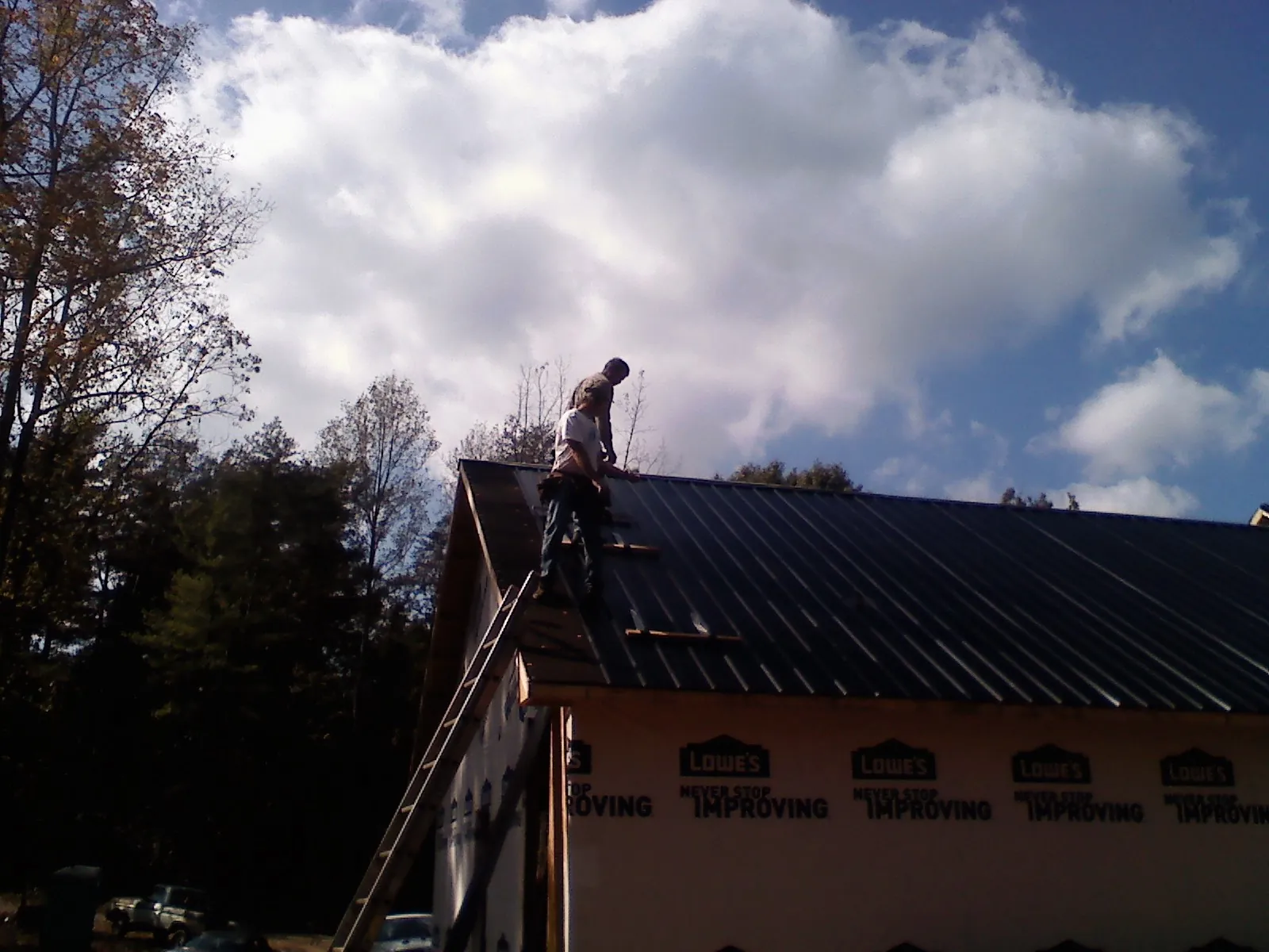 Roofer fastening dark metal panels high against a cloudy sky, from a Roof Inspection job in Nashotah