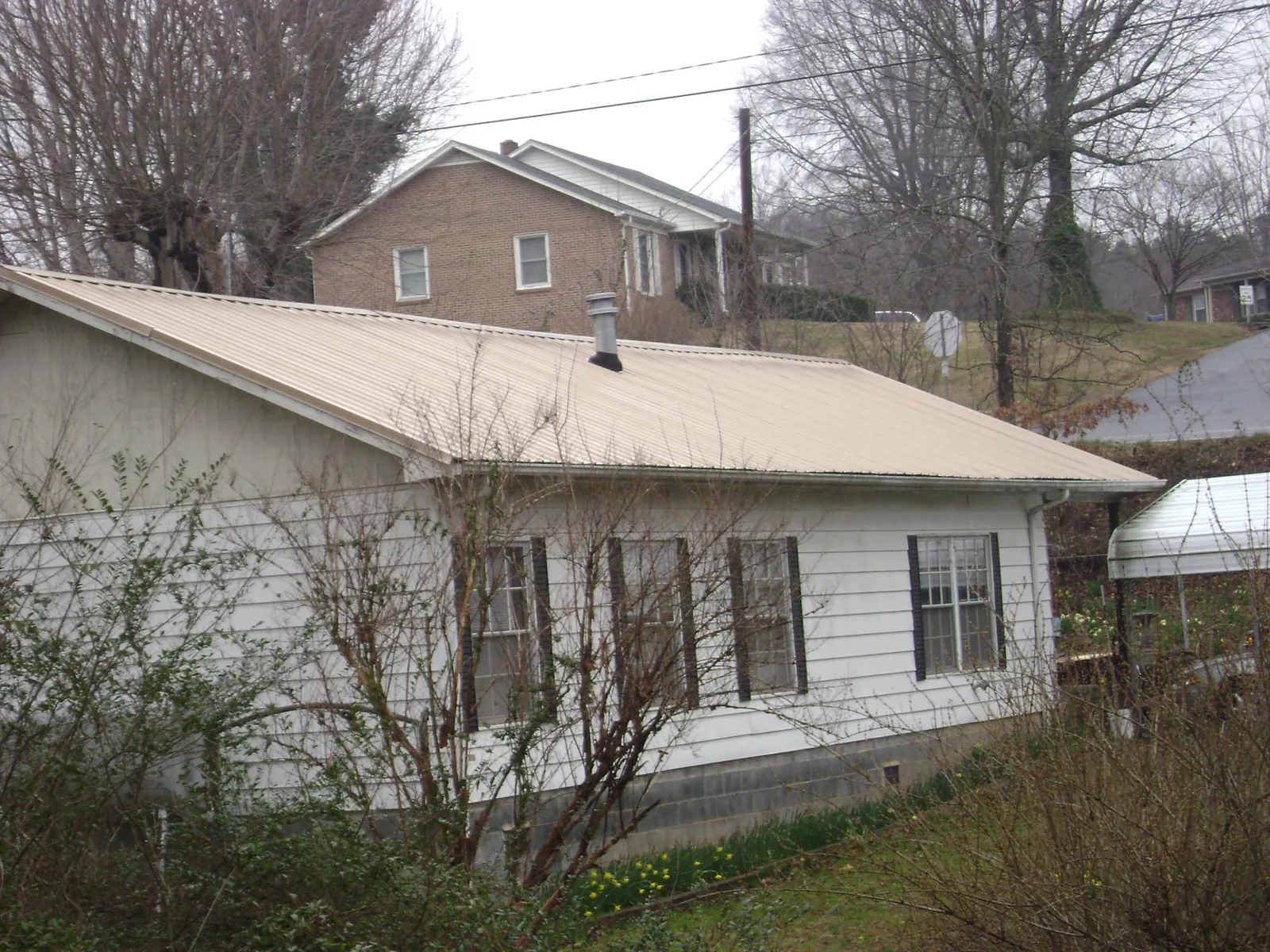 Tan metal roof on a white sided house set into a hillside — Commercial Roofing by Roofing Brothers in Nashotah