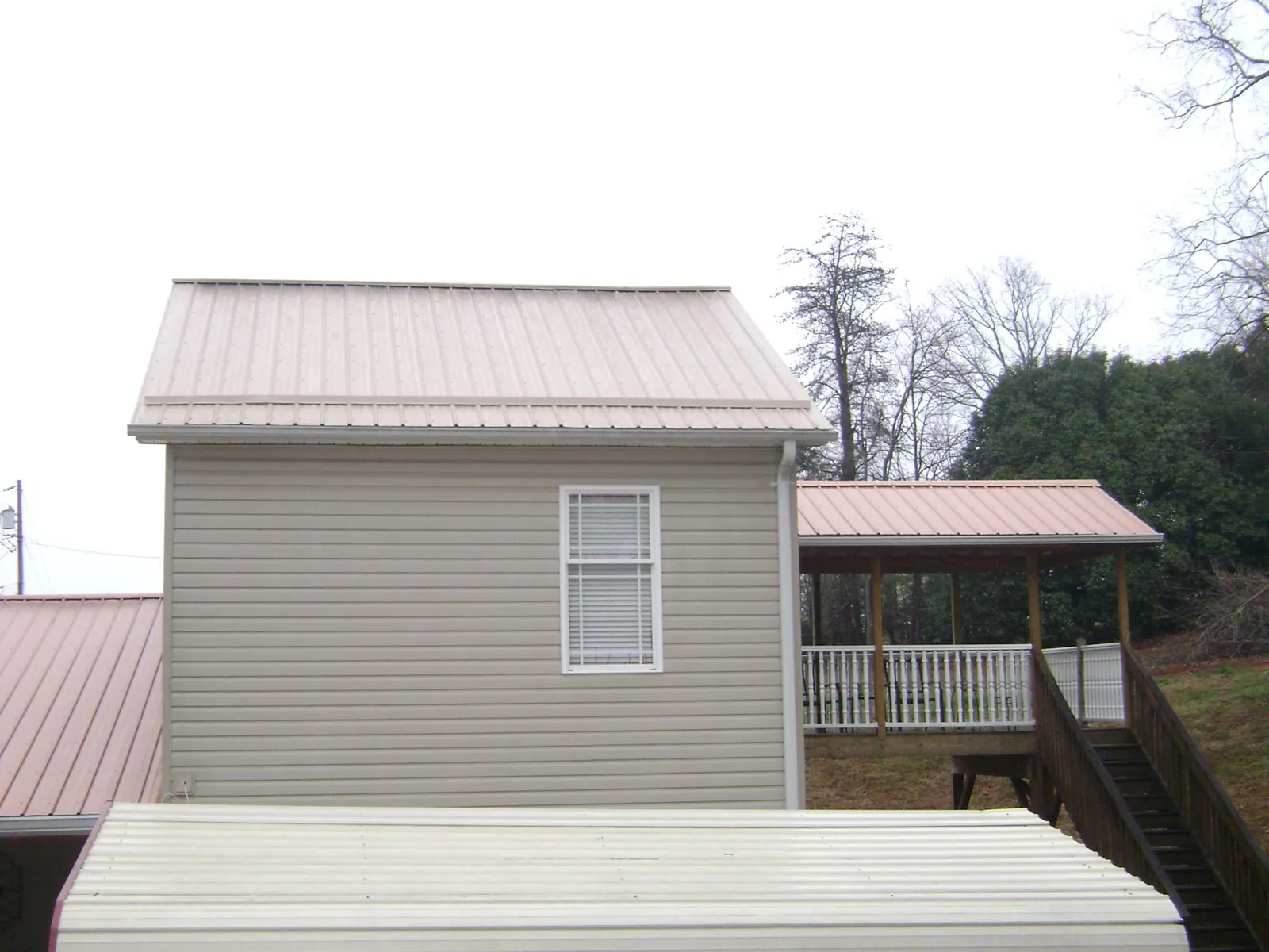 Tan metal roofs on a two story addition and attached porch, from a Roof Replacement job in Nashotah